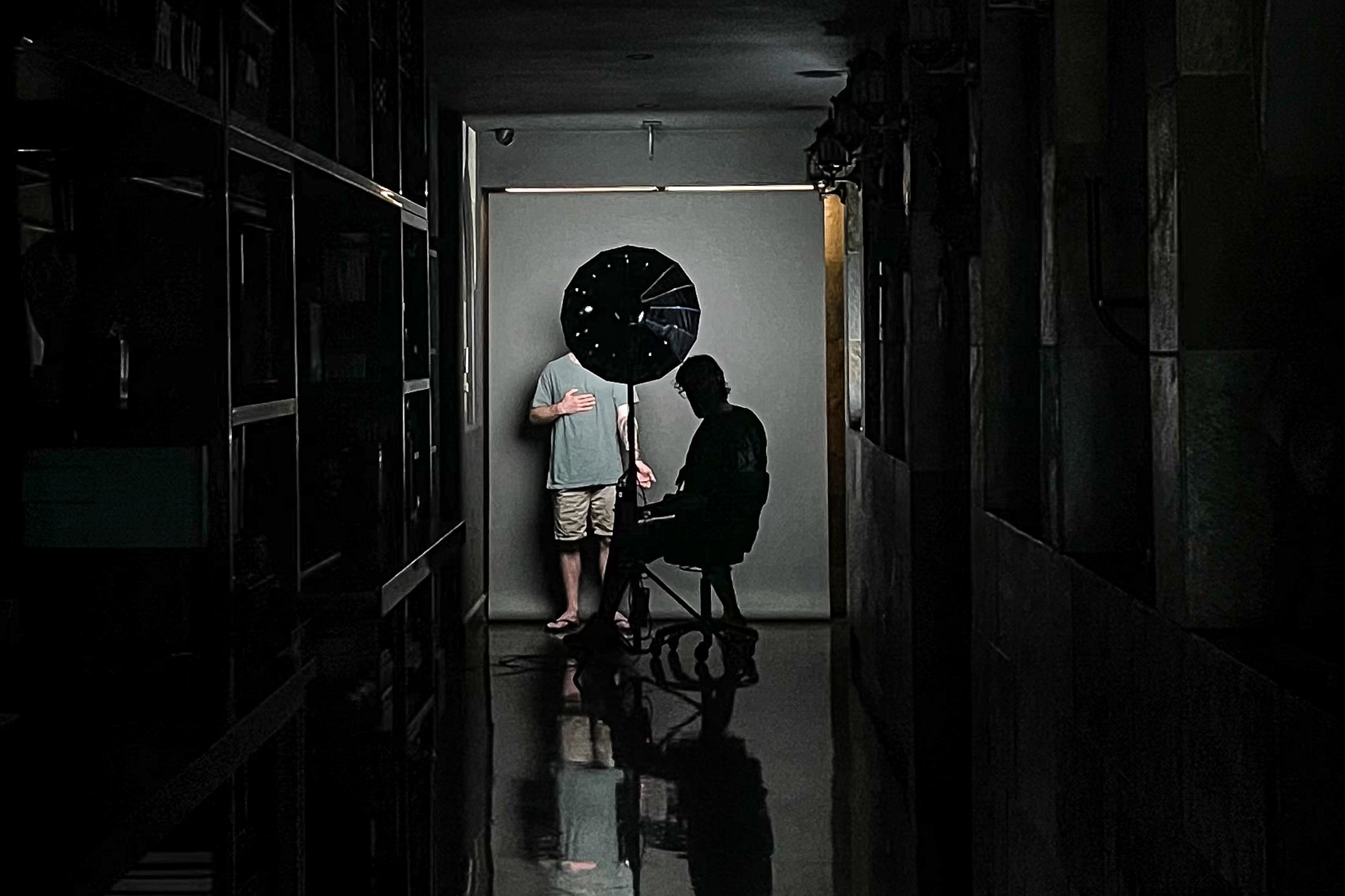 Ivan Piscopo photographing the finished tattoo on a client at the end of a session, using studio lighting in a hallway.