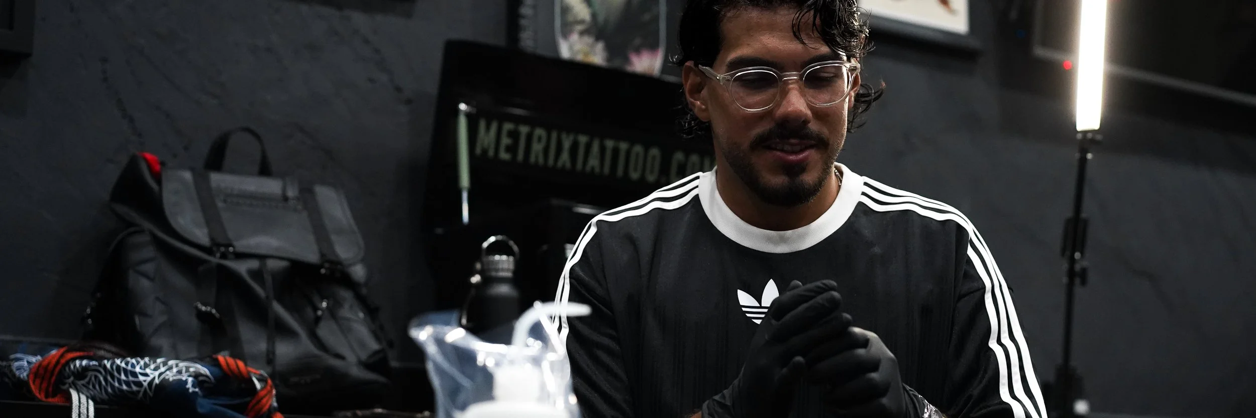 Tattoo artist Ivan Piscopo preparing for a session inside his Melbourne studio, wearing gloves and working on a black and grey tattoo.