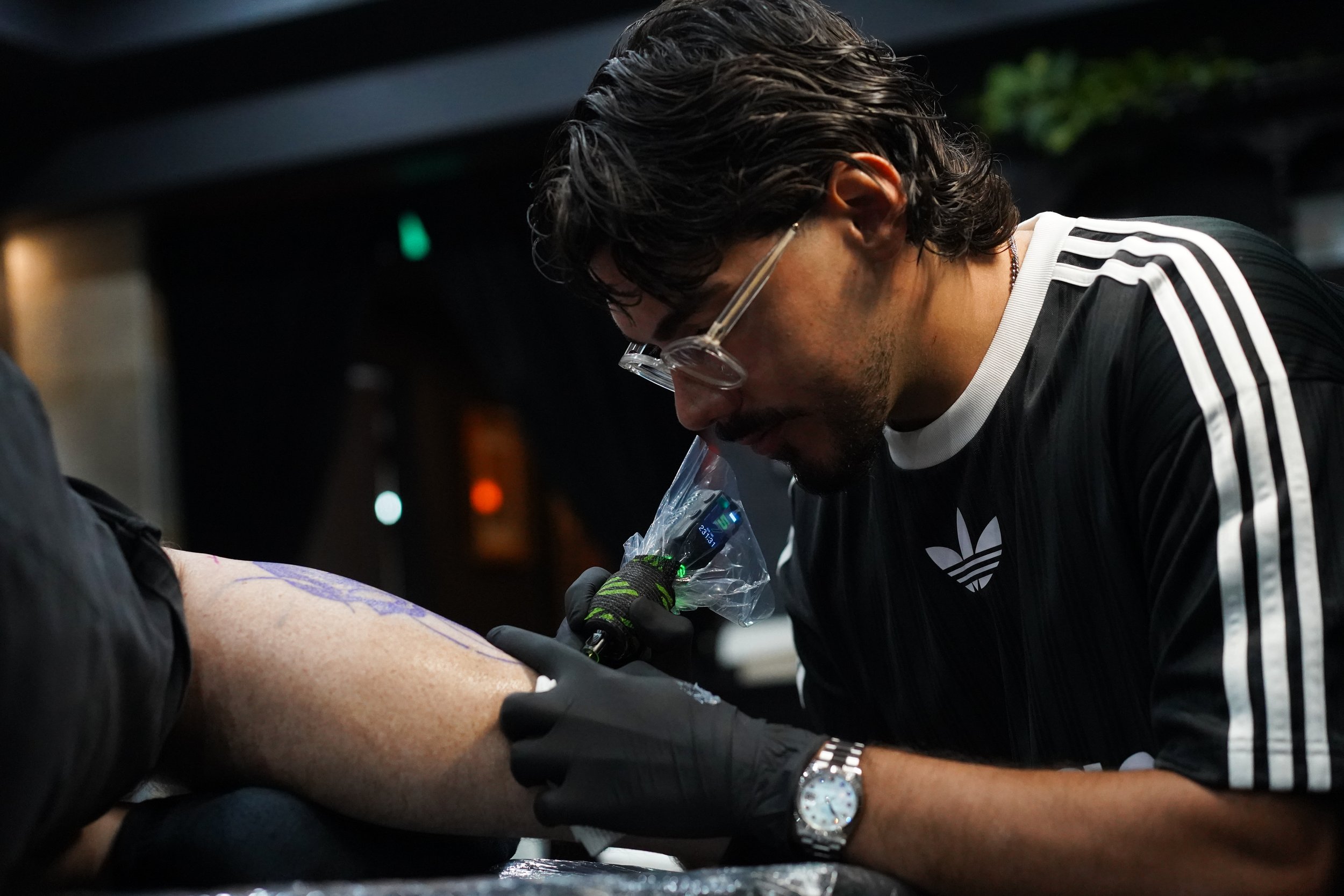 Ivan Piscopo tattooing a client’s leg in his Melbourne studio, creating a black and grey realism design with precision.