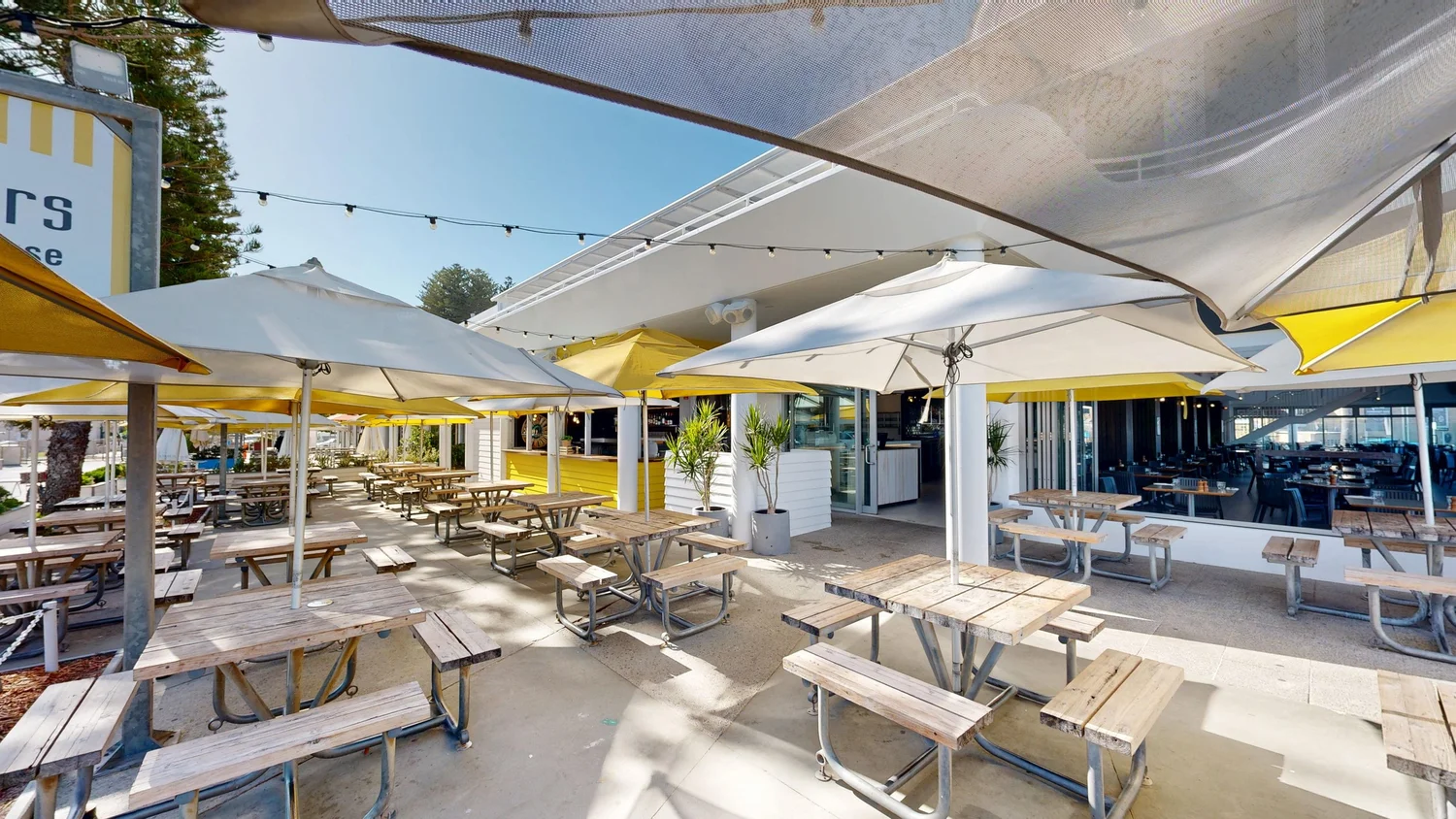 Picnic tables under umbrellas and festoon lights in the Northern Alfresco at Bathers Beach House