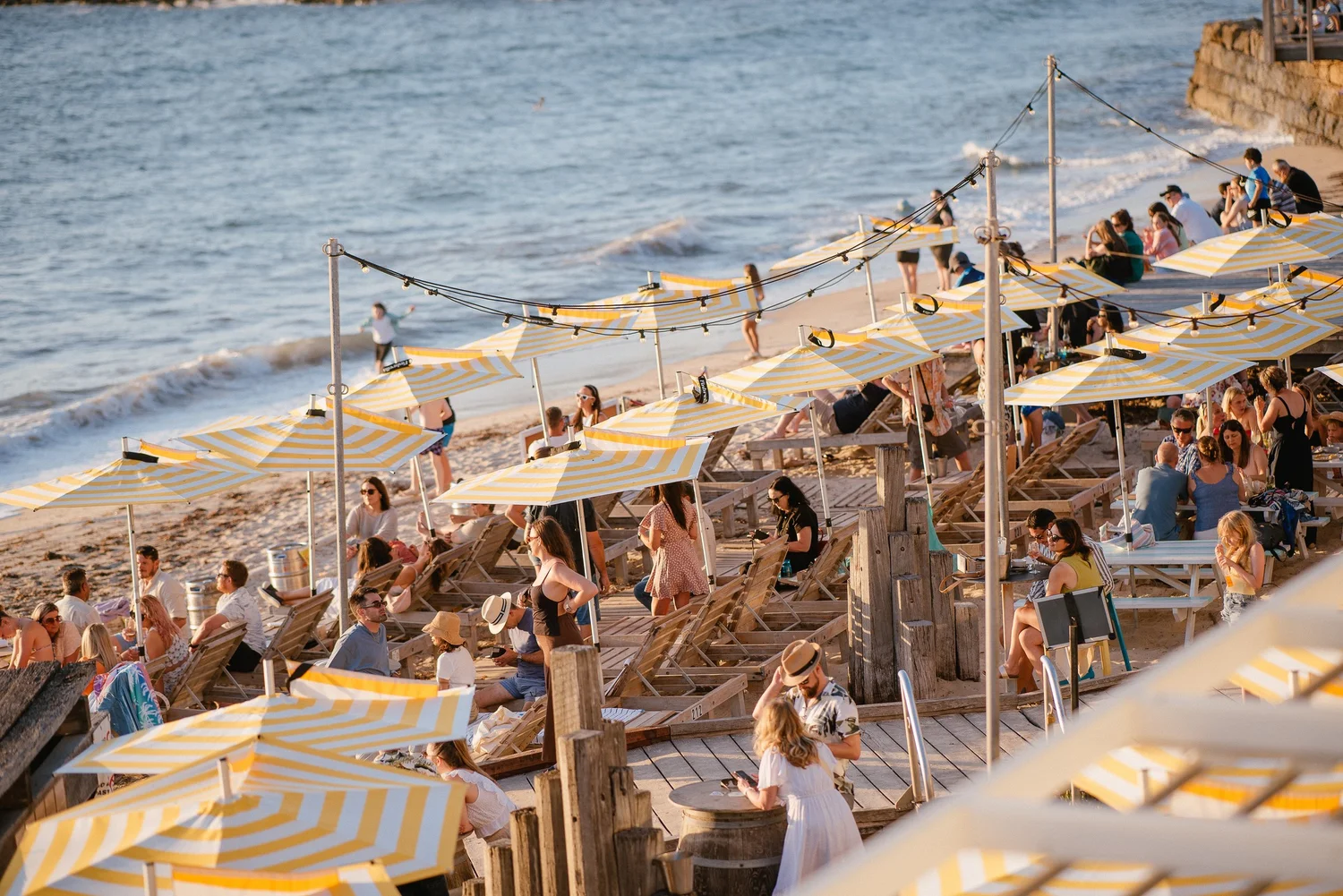 Guests on the beach lounges and loungers on the sand at Bathers Beach House at sunset