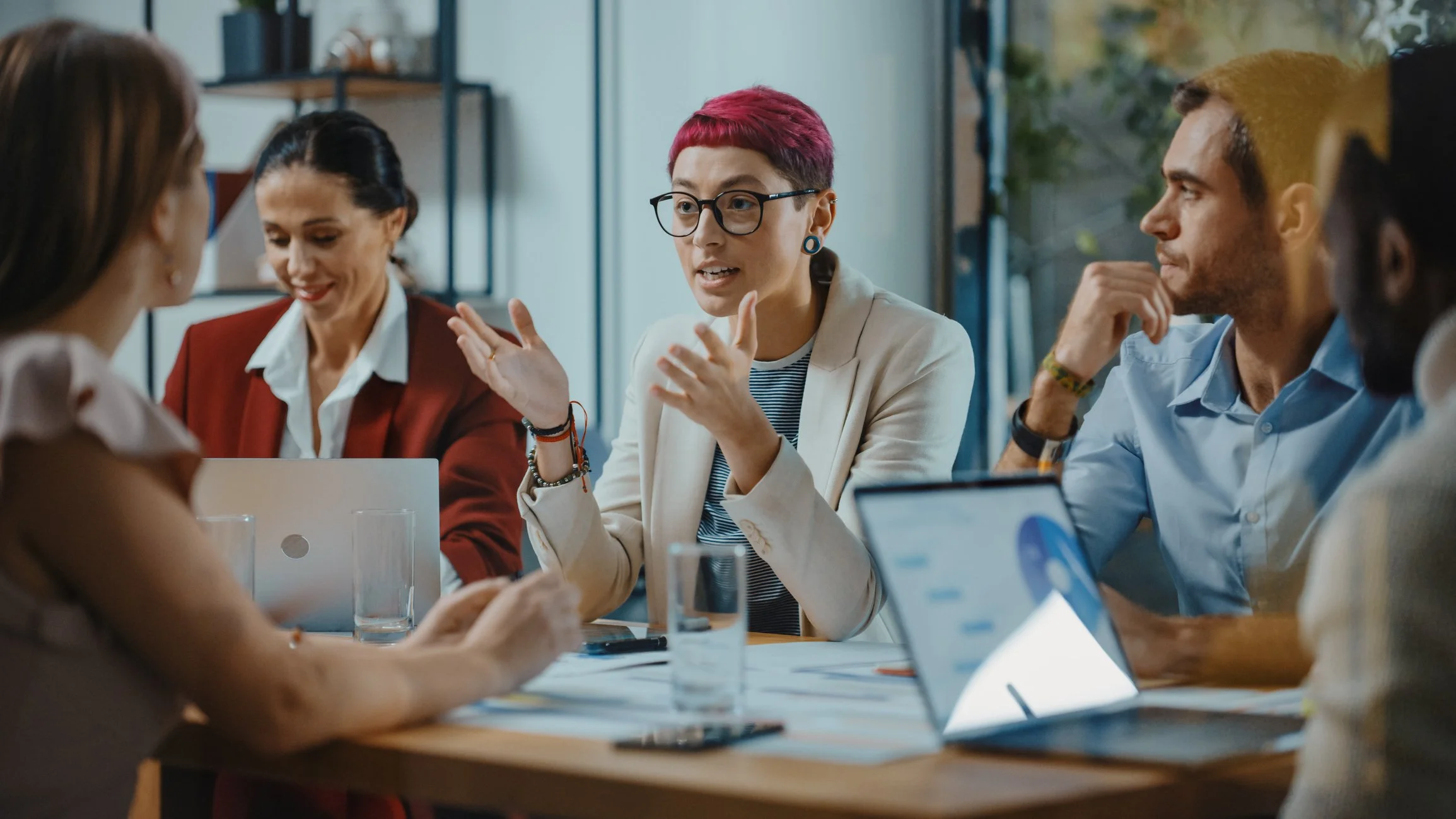 A group of people having a discussion in a meeting room with laptops and tablets.