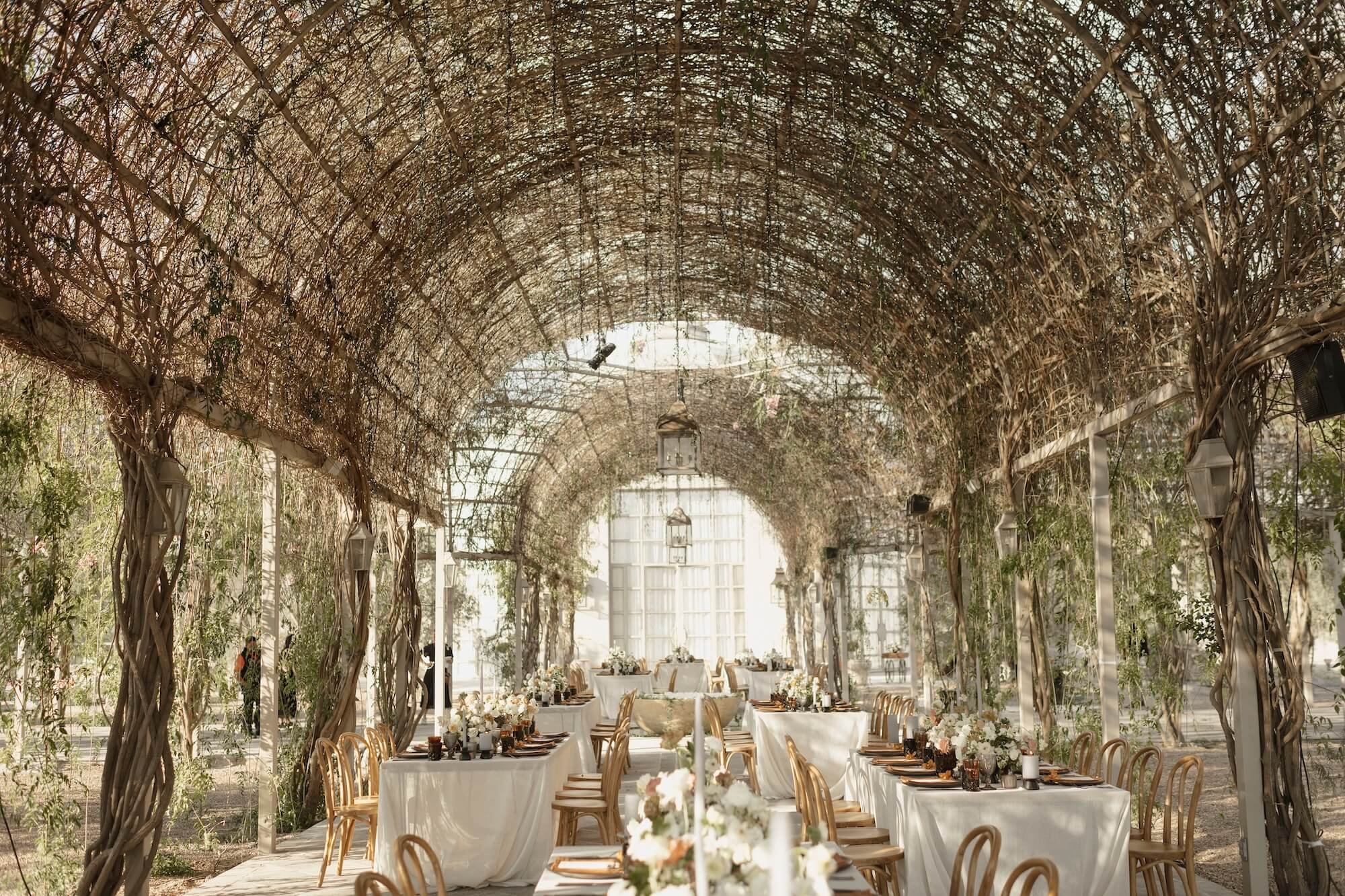 Elegant outdoor wedding reception setup under a vine-covered archway with tables, white tablecloths, and floral centerpieces