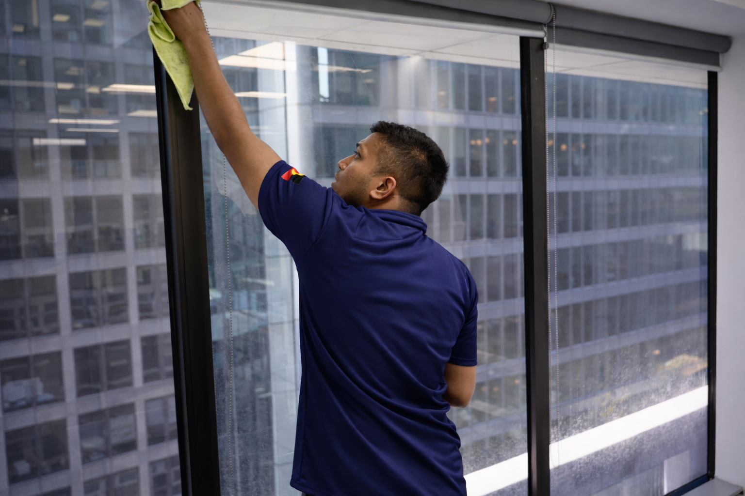 A man cleaning a large glass window with a yellow cloth inside a modern office building.