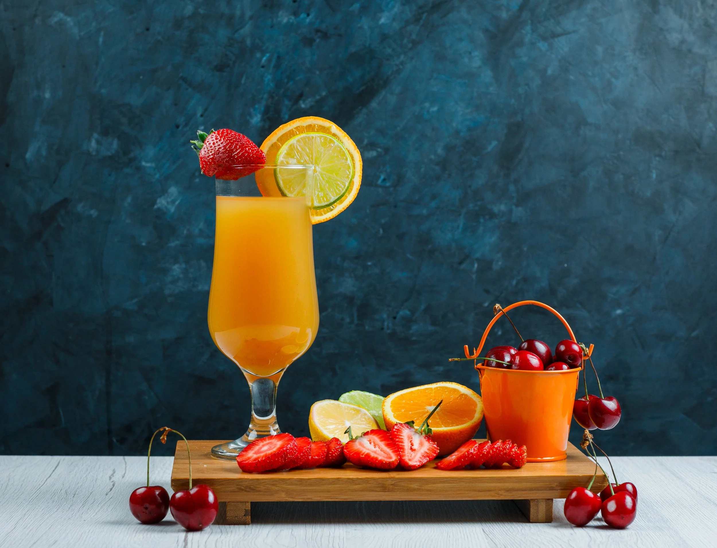 orange-juice-goblet-with-citrus-fruits-strawberry-cherry-cutting-board-side-view-wooden-grungy-blue-background.jpg