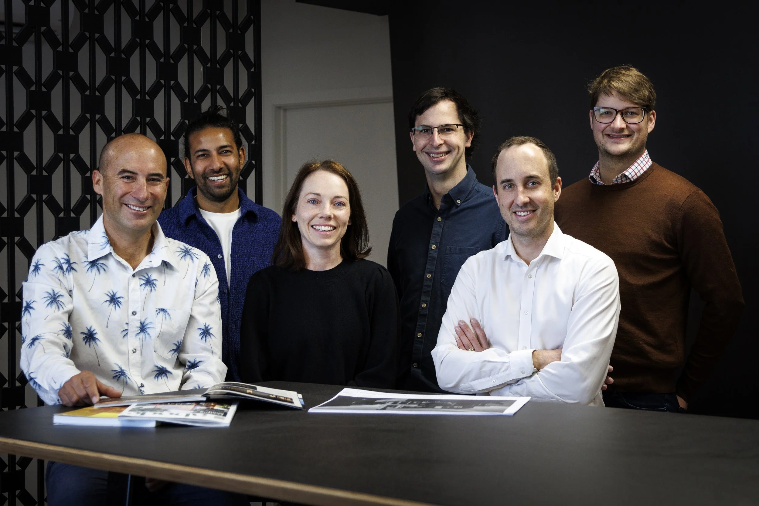 Group of six diverse professionals together in a modern office setting in front of an Autex Cascade acoustic screen.