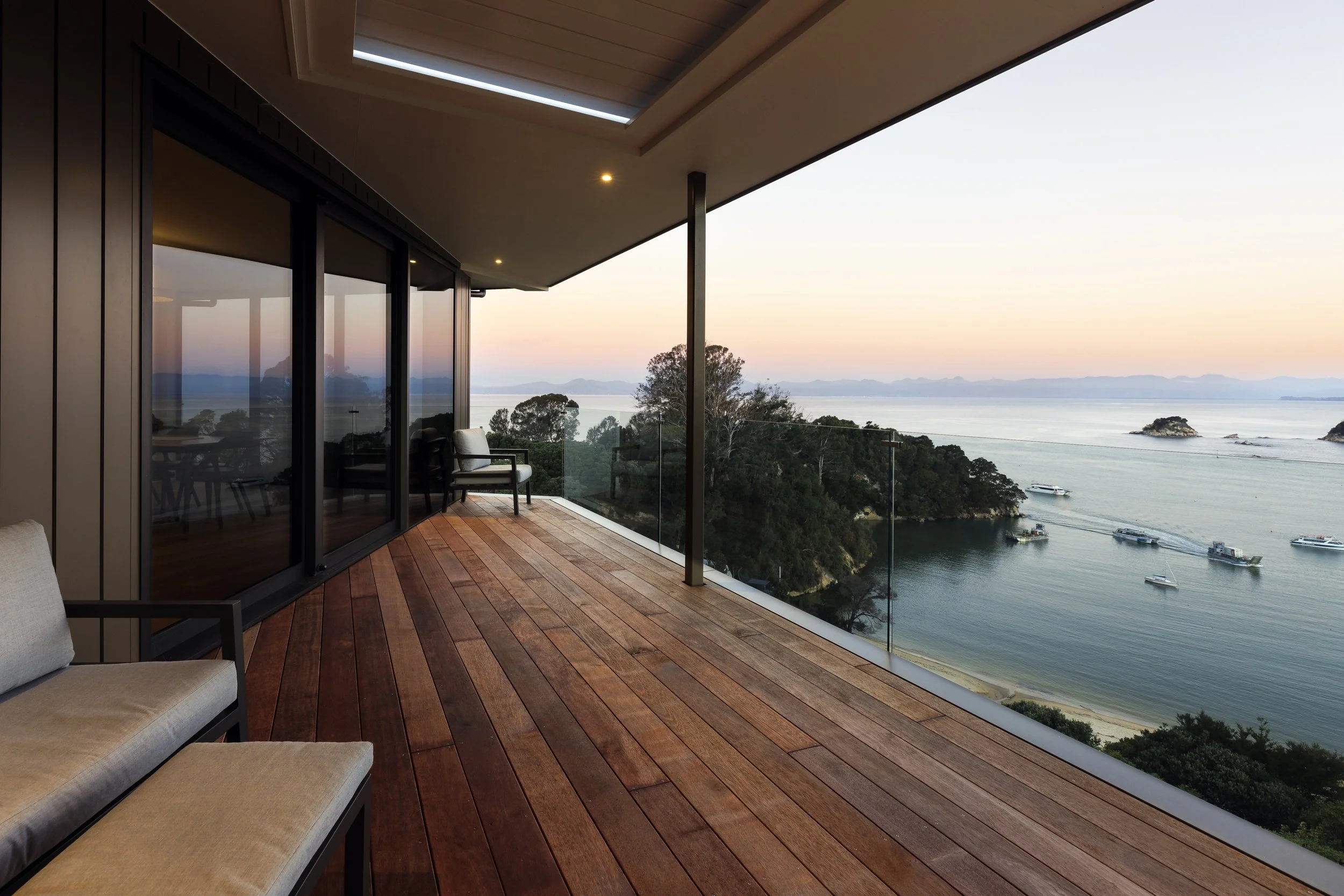 Modern apartment balcony overlooking calm water and boats, with trees and islands in the background during sunset.