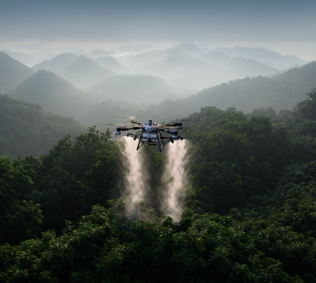 A drone flying over a lush green forest, dispersing water in a mist or spray, with misty mountains in the background.