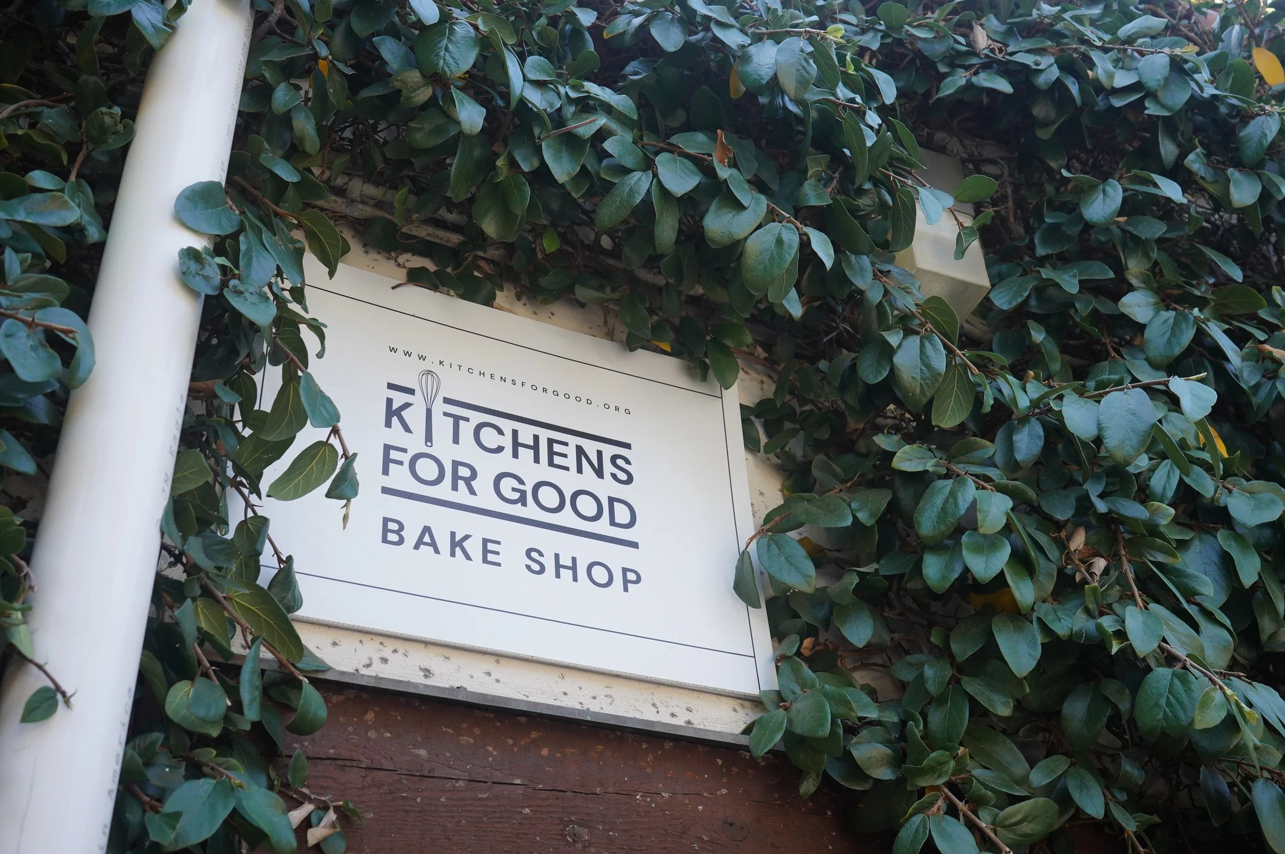 Sign for Kitchens for Good Bake Shop, surrounded by green leafy vines.