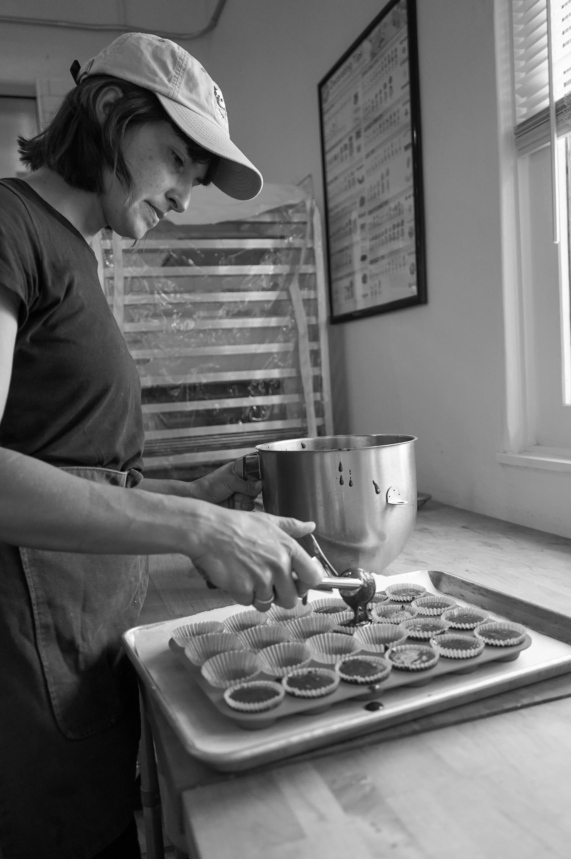 Woman in a baseball cap filling cupcake liners with filling in The Delicate Squash's bakery kitchen.