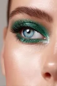 Close-up of a woman's eye with green glitter eyeshadow and long lashes.