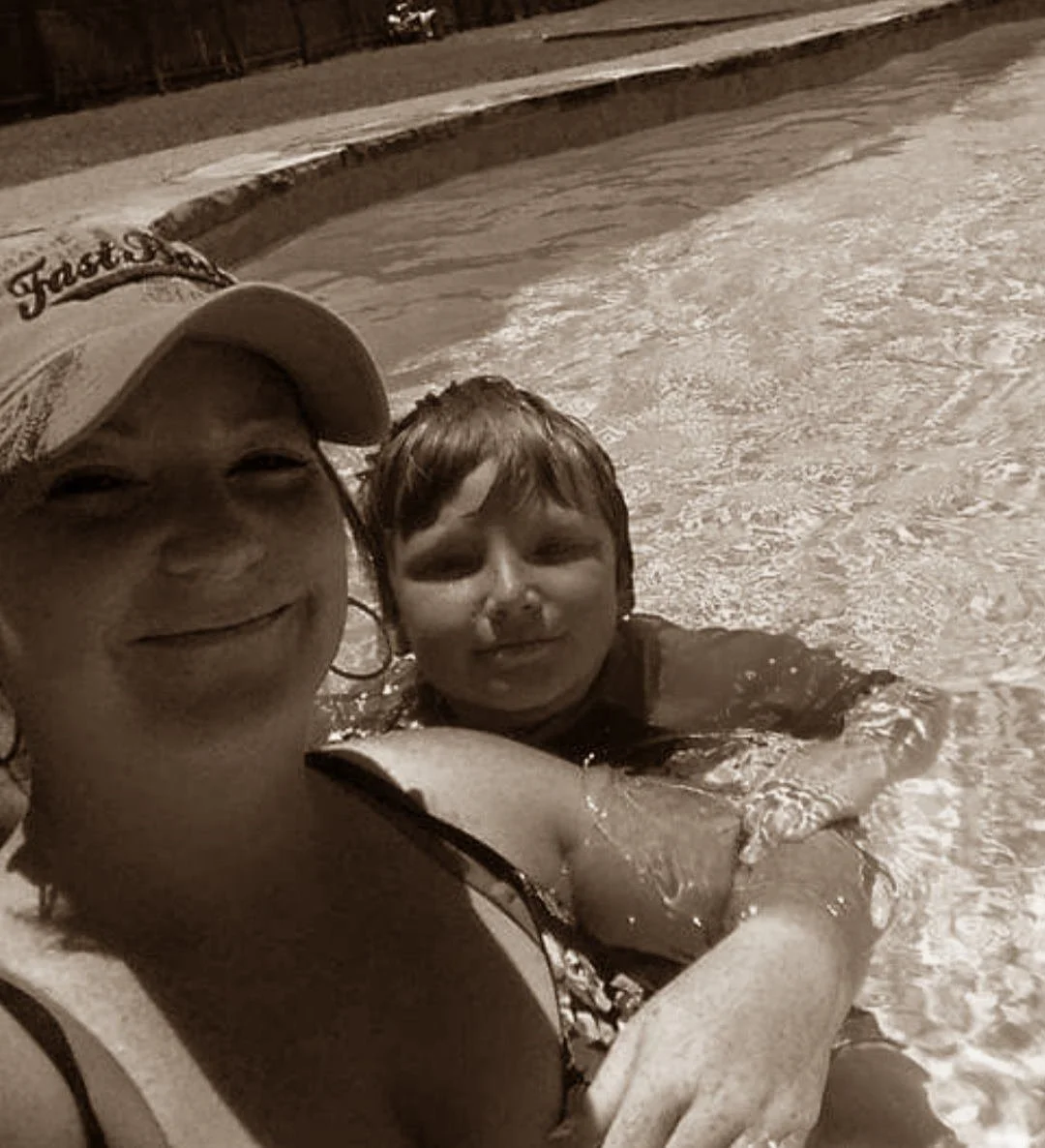 A woman and a young boy enjoying a swim in a pool in daytime, smiling and close to each other.