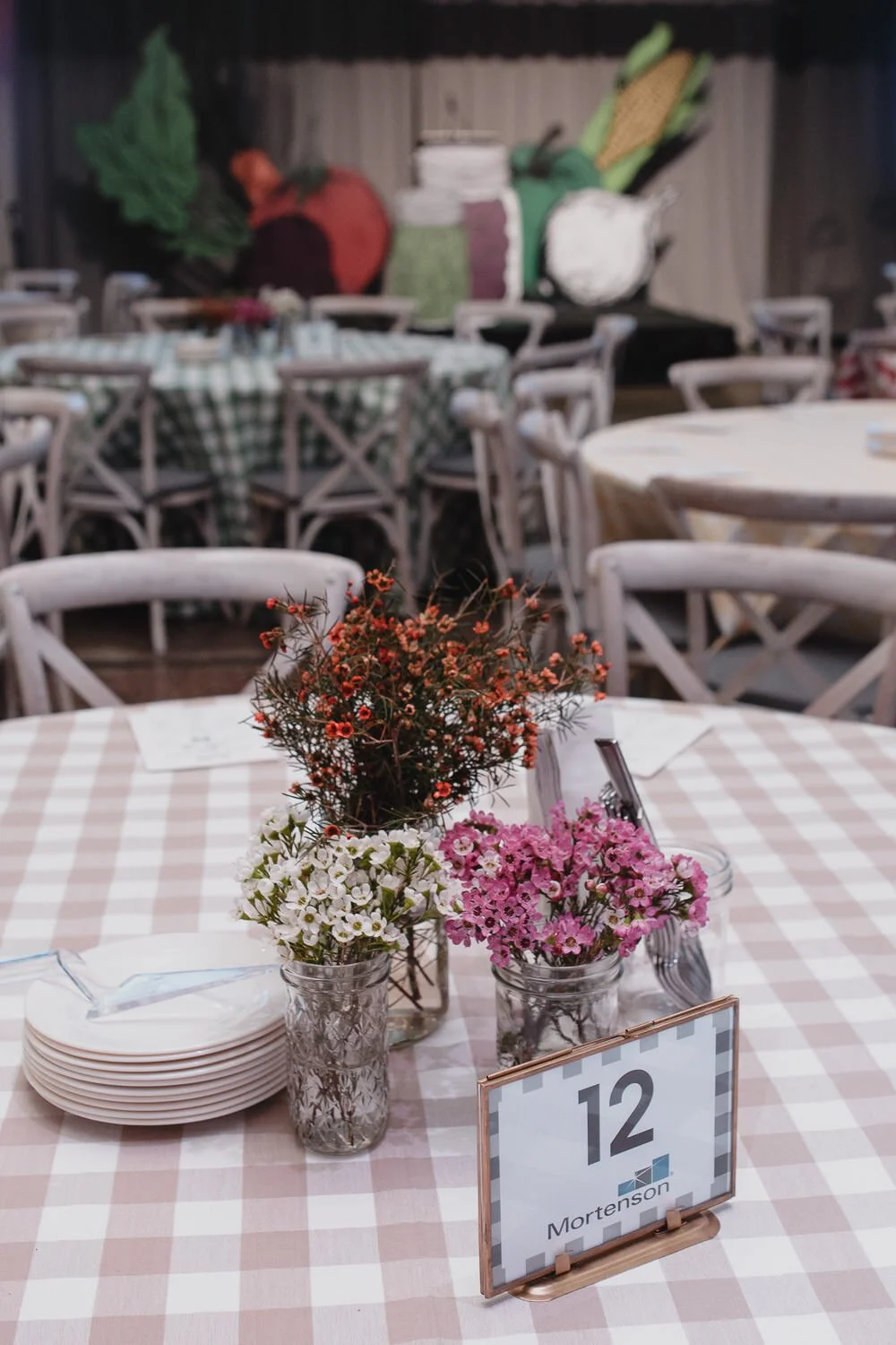 table with pink plaid table cloth and orange White and pink flowers in mason jars for Americana farm themed event