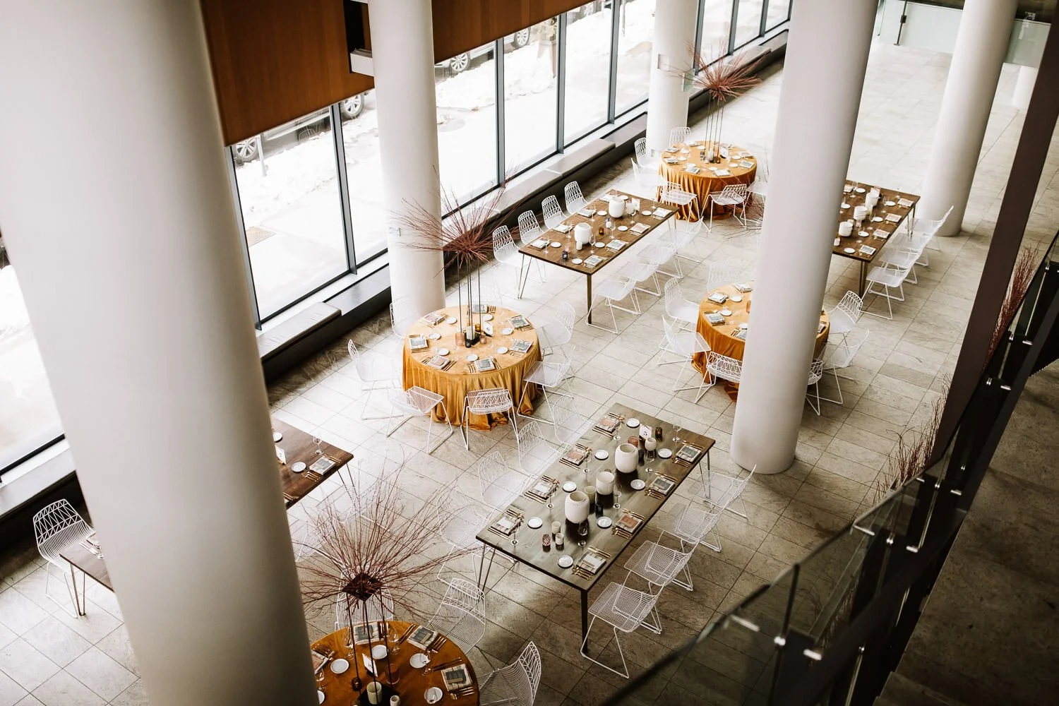 aerial view of modern wedding tables set up for the reception with round tables with mustard yellow table cloths and rectangular tables set between white pillars and glass.