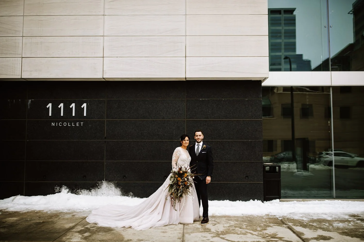 bride wearing long-sleeved lace gown with the groom wearing a dark charcoal grey suit. bouquet of dried flowers and feathers