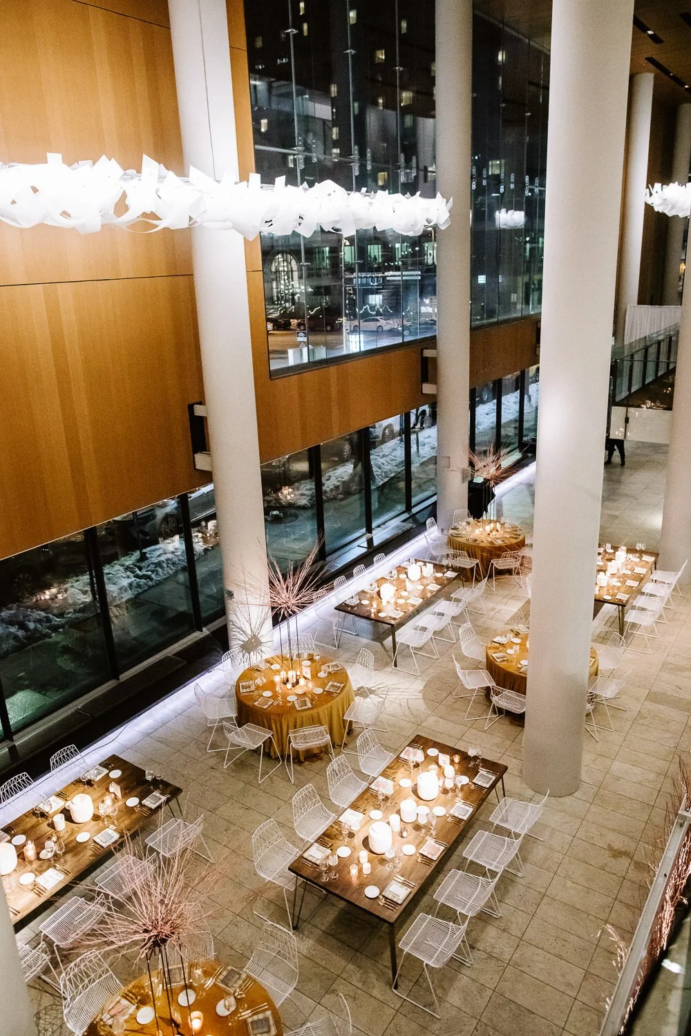 aerial view of modern wedding tables set up for the reception with round tables with mustard yellow table cloths and rectangular tables set between white pillars and glass.