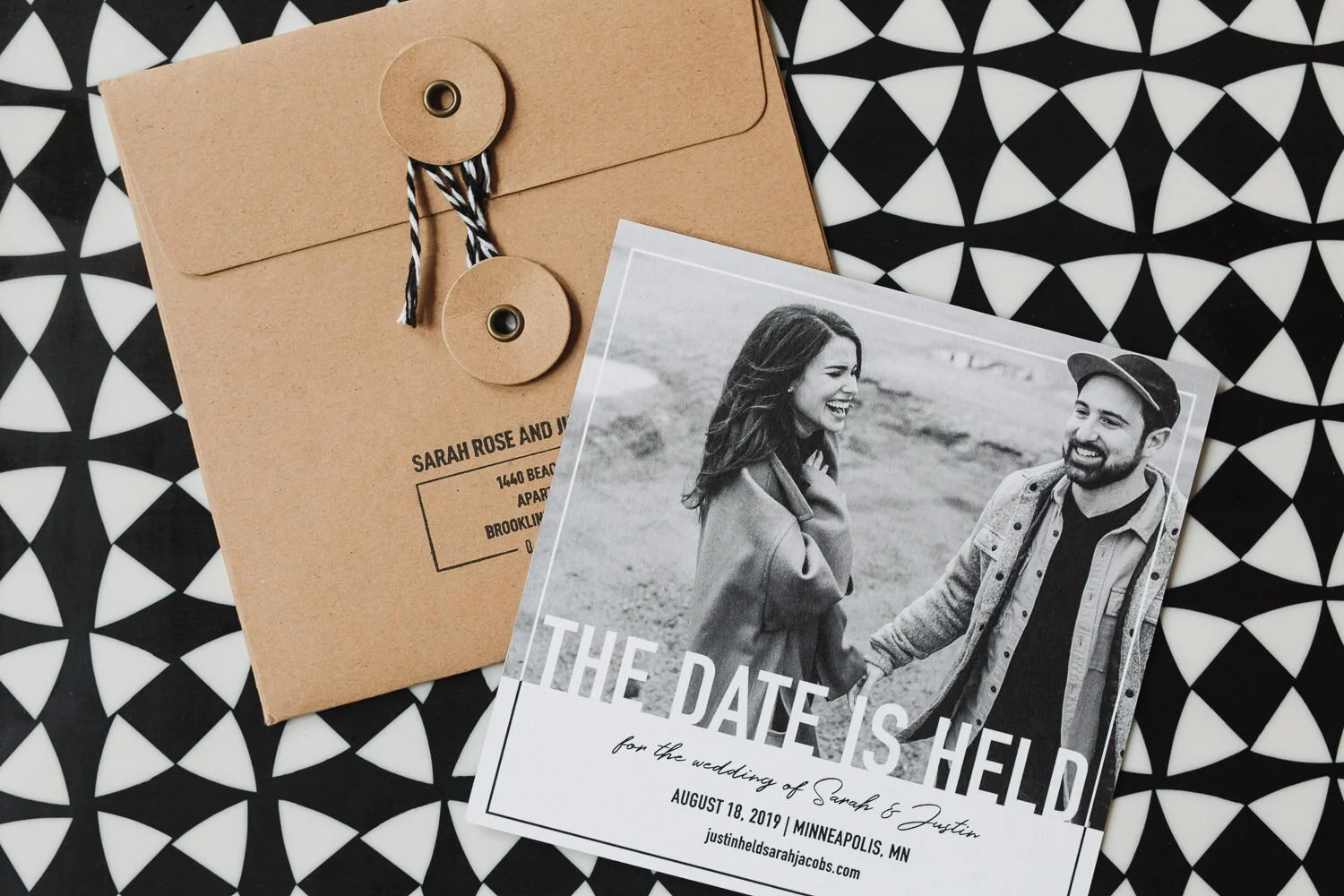 black and white save the date square card with a black and white photo of bride and groom with a natural brown envelope and black and white string on top of black and white geometric design.