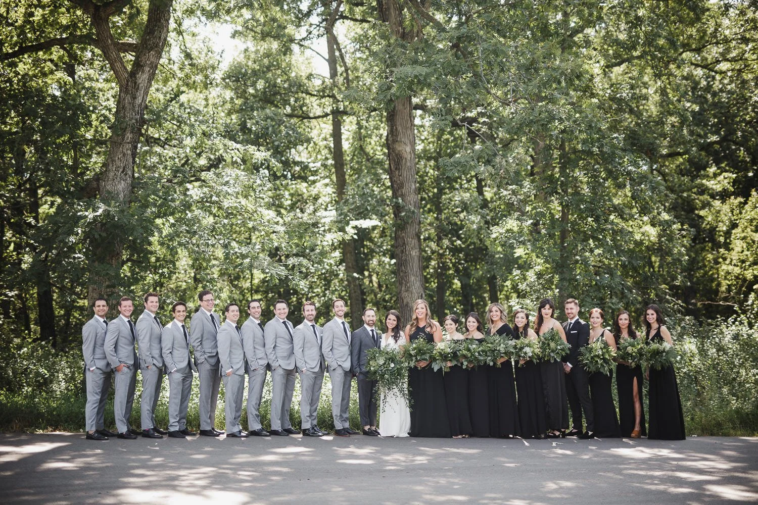 wedding party of groomsmen in light grey suits and bridesmaids in black dresses