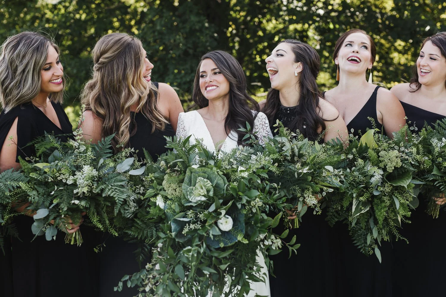 bride and bridesmaids laughing with large all green bouquets