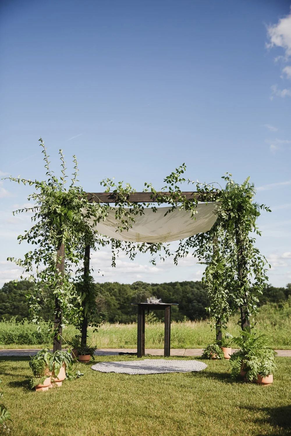 chuppah with white canopy, wood legs, and all gree florals