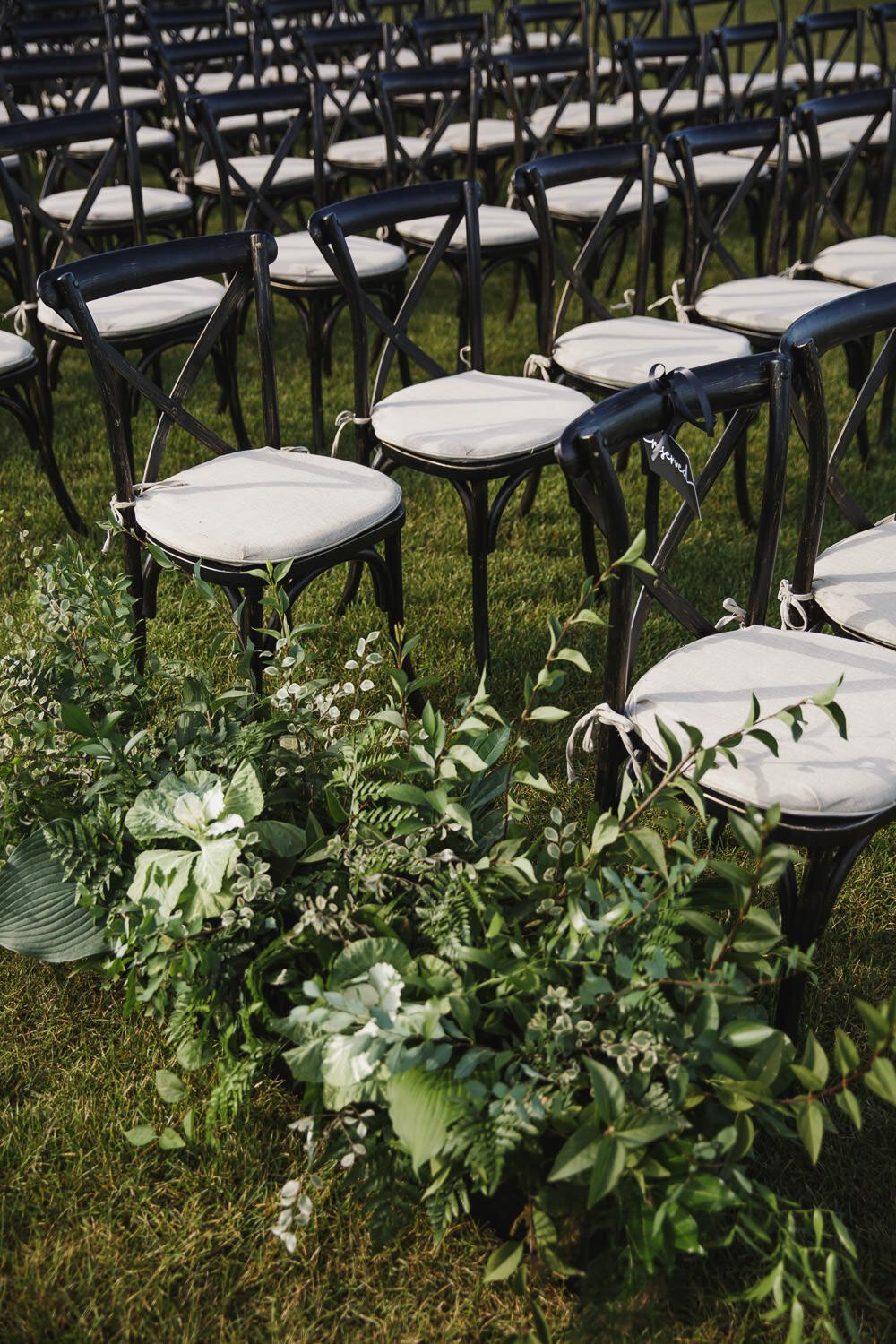black and white chairs set up for wedding ceremony with all green aisle bouquets.