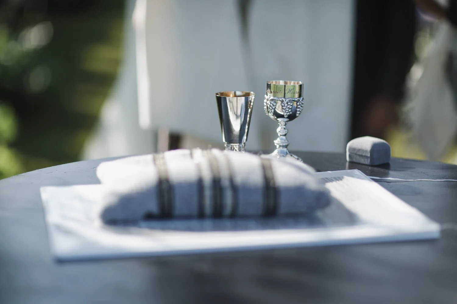 Jewish wedding ceremony details with glass wrapped in cloth and pewter wine cups and ring box.