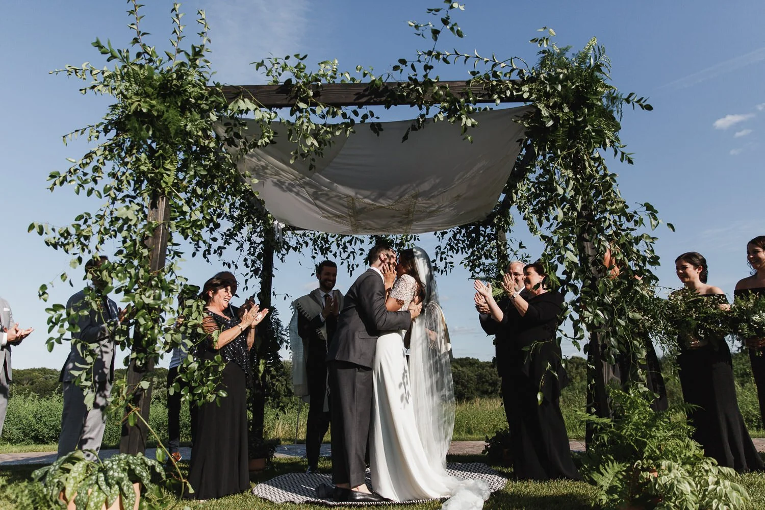 Jewish wedding ceremony kiss the bride with family clapping in black dresses and grey suits