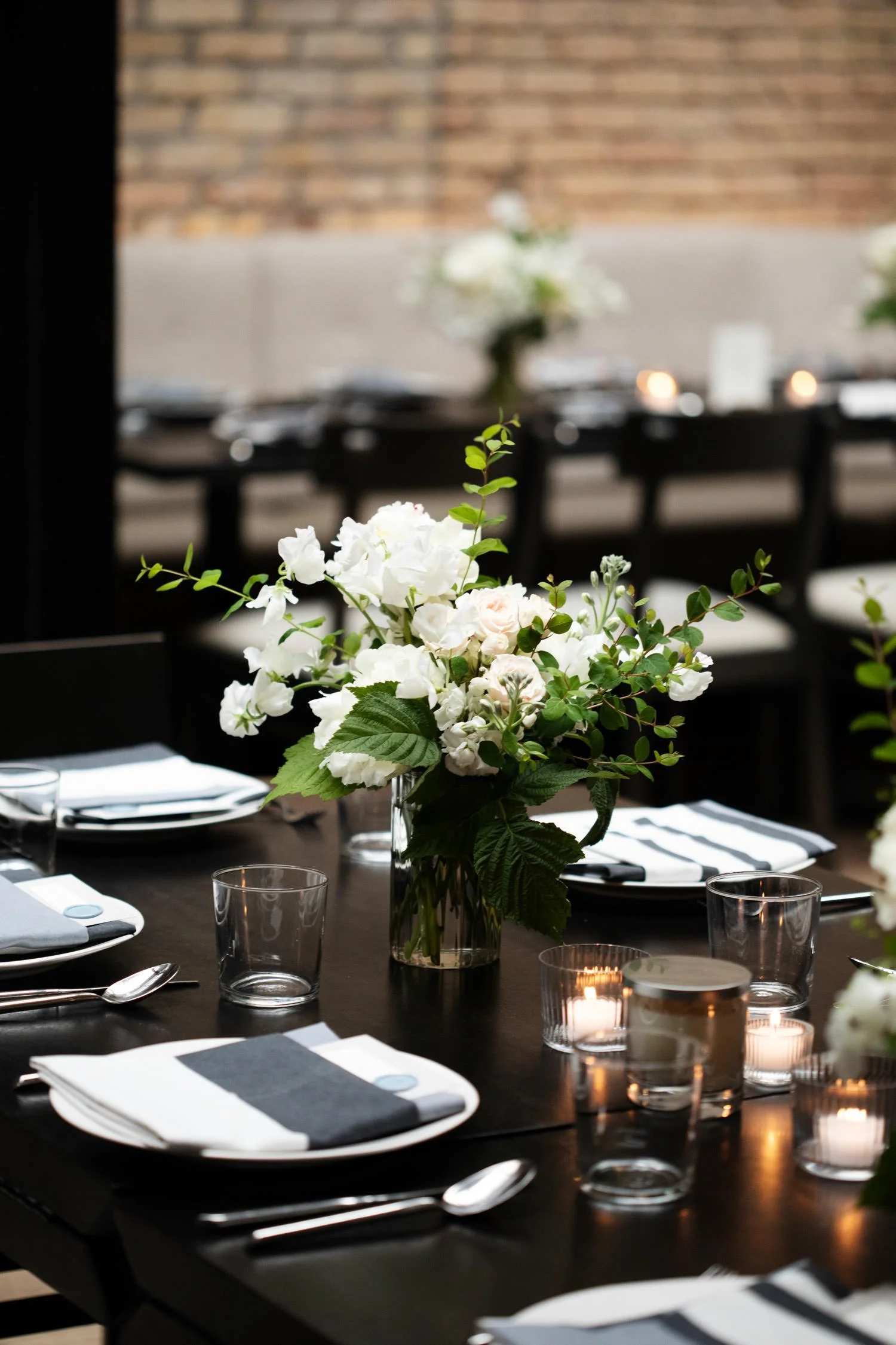 Black long tables and chairs with white tableware and custom-designed menu stationary. White daisies are placed perfectly. Minneapolis rehearsal dinner, Spoon and Stable restaurant, Designed by Rocket Science Events.