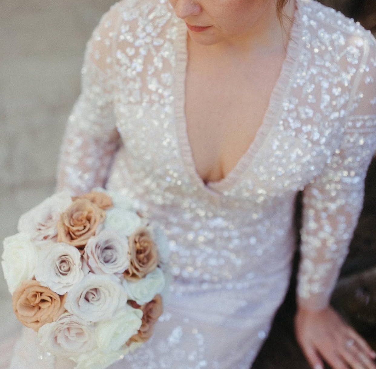 A woman in a sparkly, sheer dress holds a bouquet of white and blush roses.