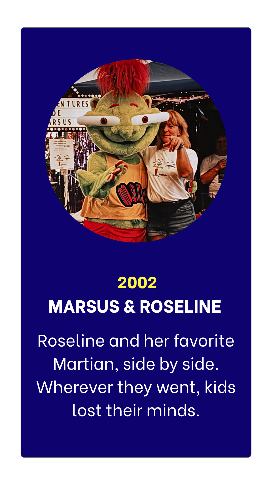 A woman and a mascot dressed as a Martian posing together at a fair or festival, with a sign in the background.