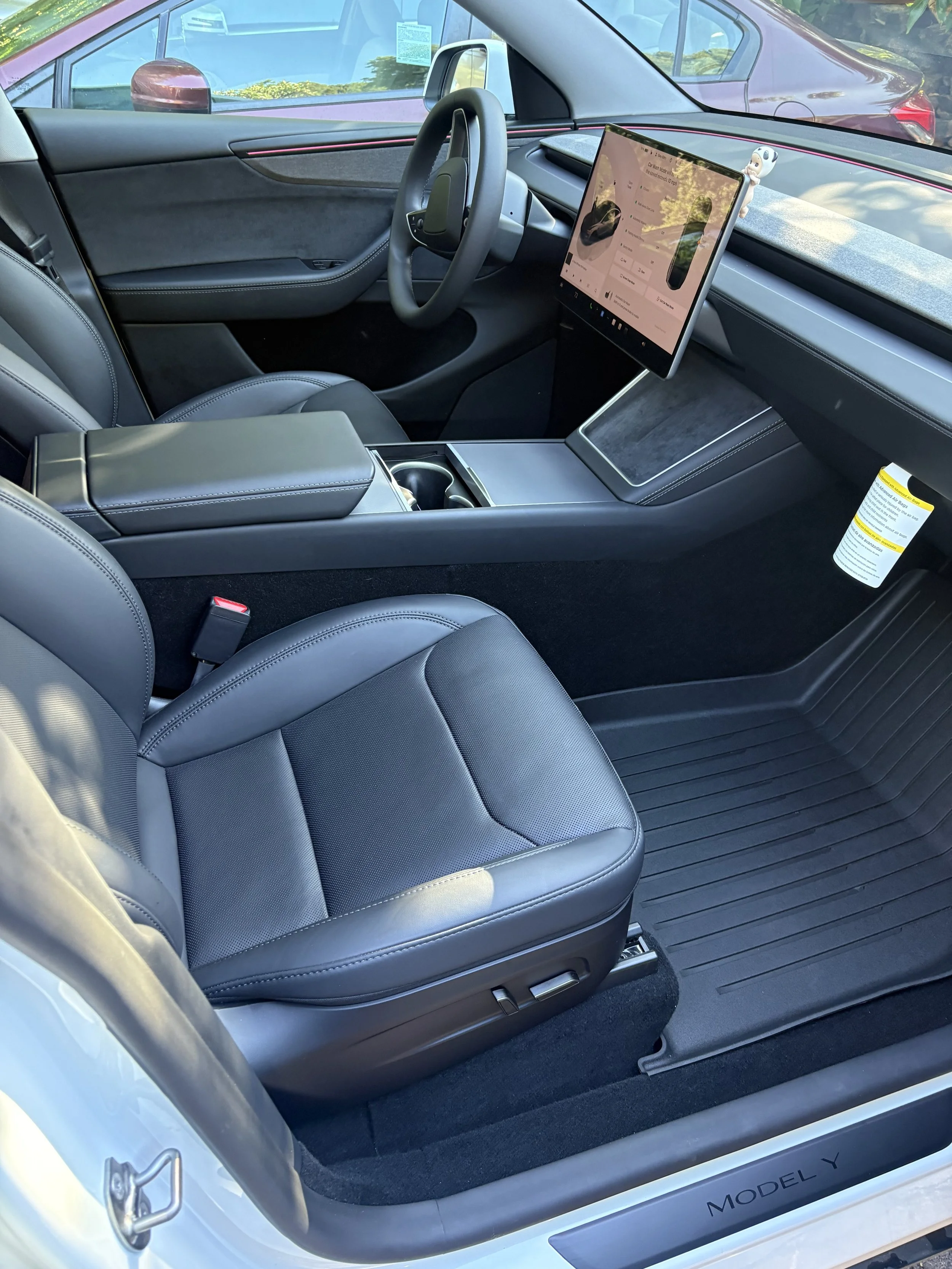 The interior of a modern electric vehicle, showing the driver's seat, a digital dashboard, and a large touchscreen display on the dashboard, with a small dog figurine on top of the display.