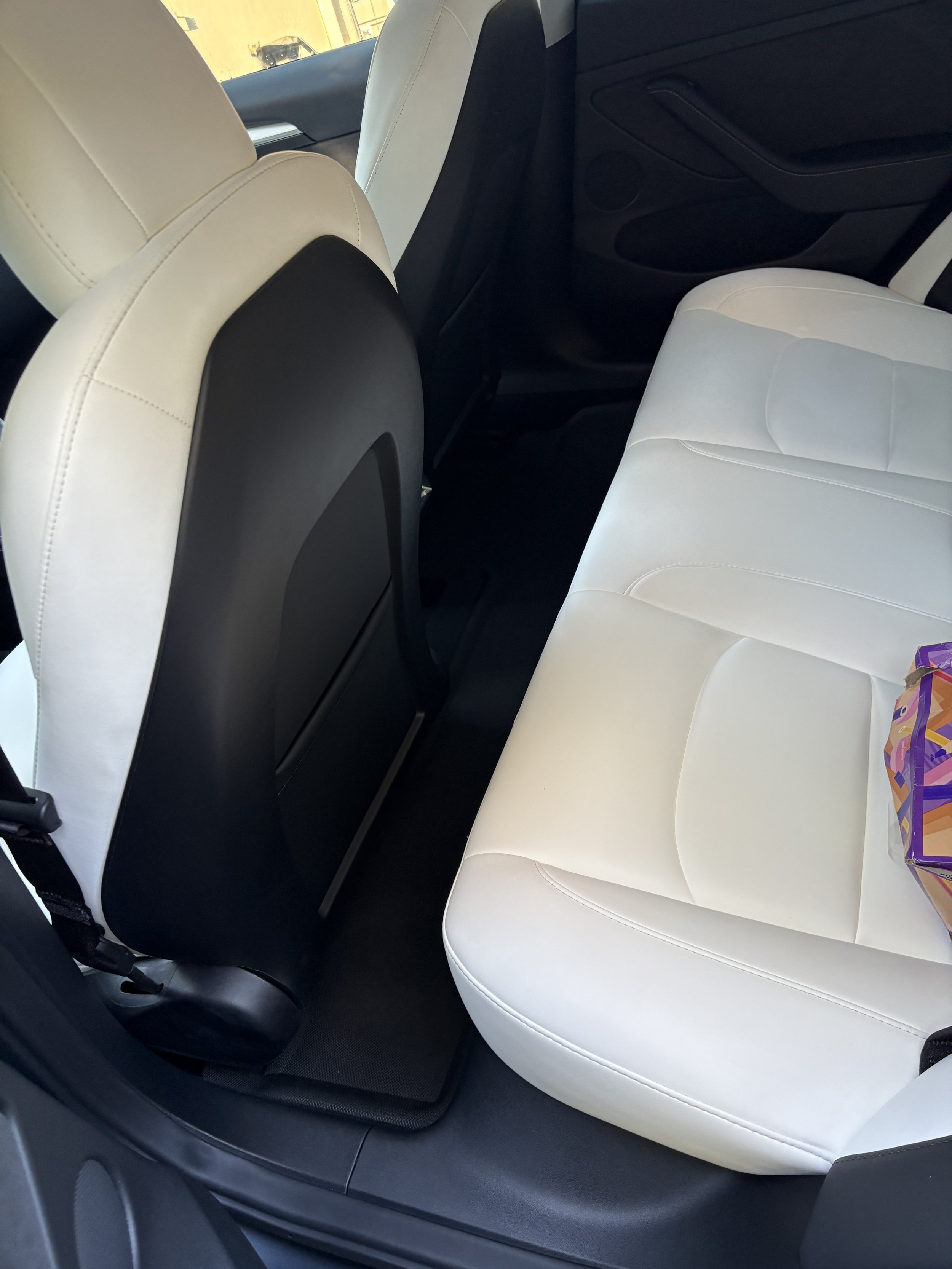 Inside view of a car showing the back seat area with white leather seats, a black seat back, and part of the door panel.