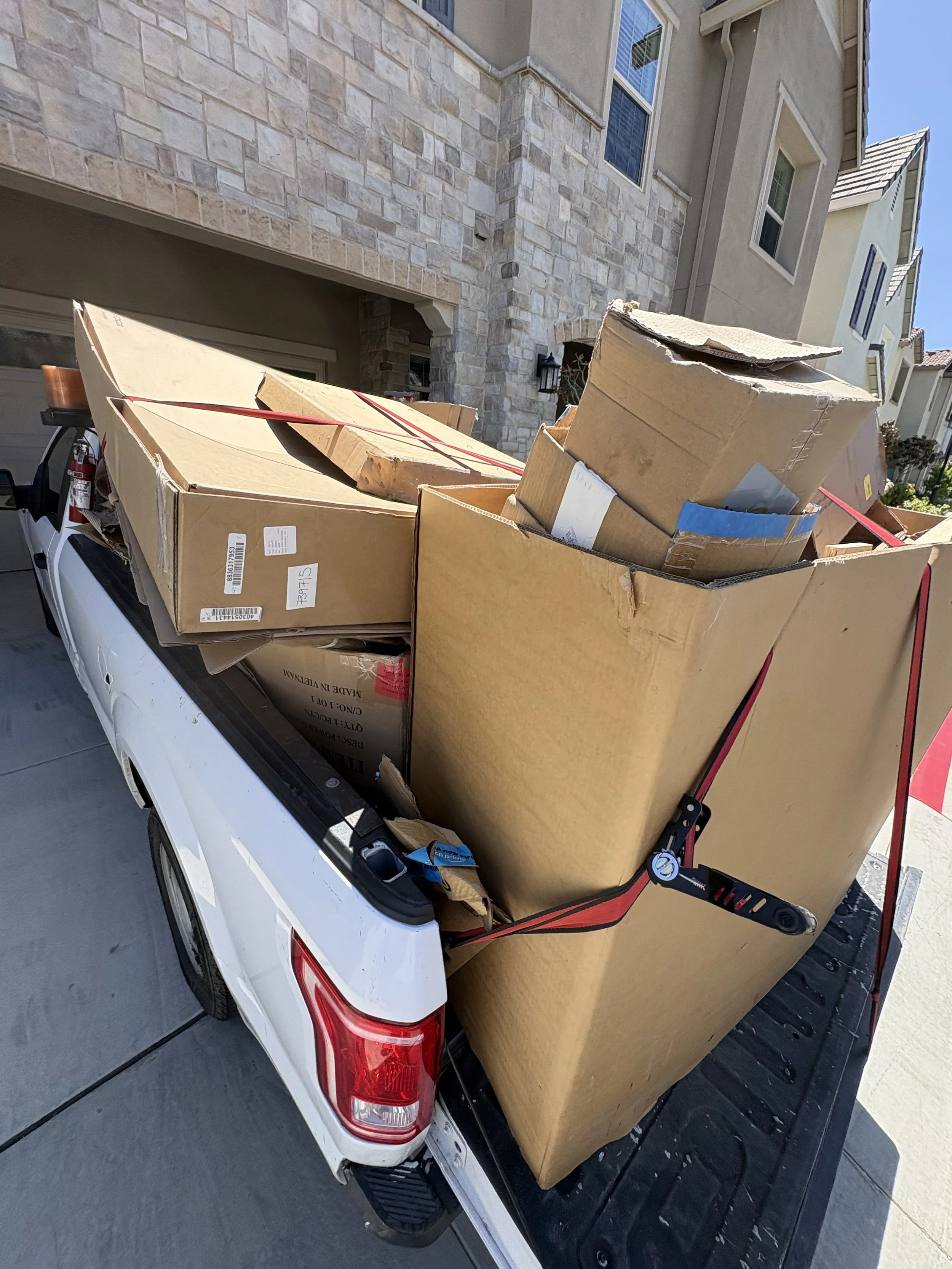 Pickup truck loaded with large cardboard boxes during daytime outside residential houses.