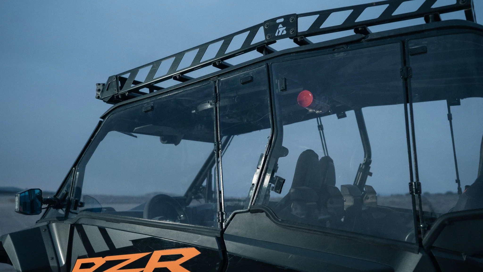 Close-up of a black off-road vehicle with a protective windshield and a red warning light, set against a blue sky.