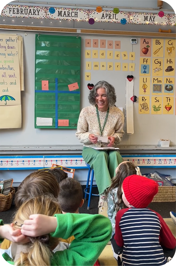 Kristen Corwin smiling warmly in her kindergarten classroom, engaging with her seated students.