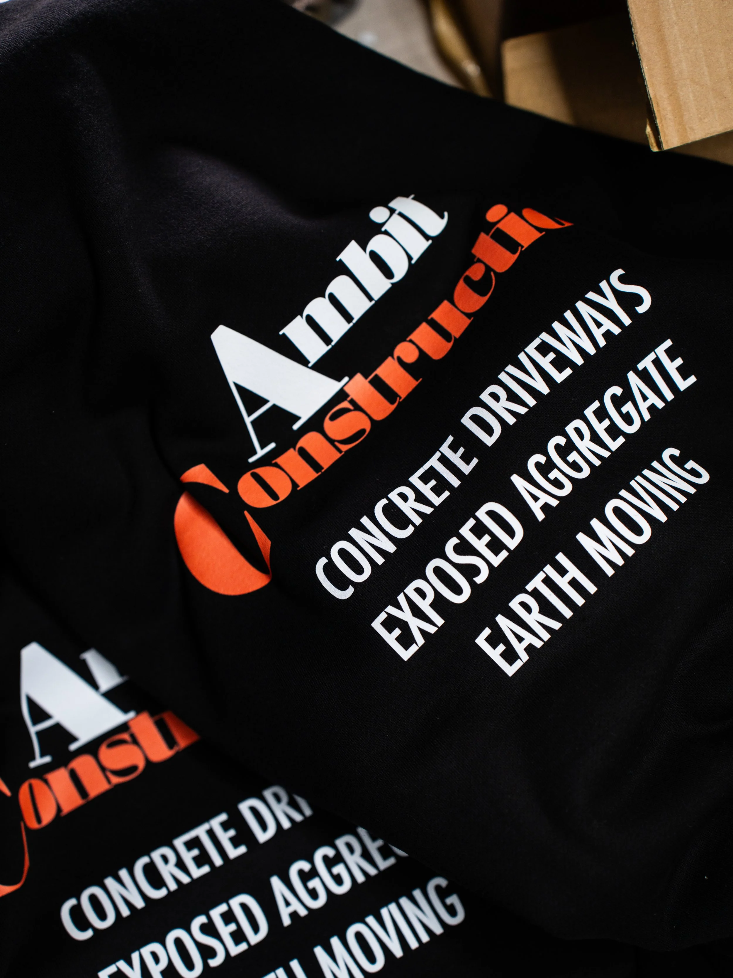 Black tote bag with white and orange text about concrete design and earth-moving services.
