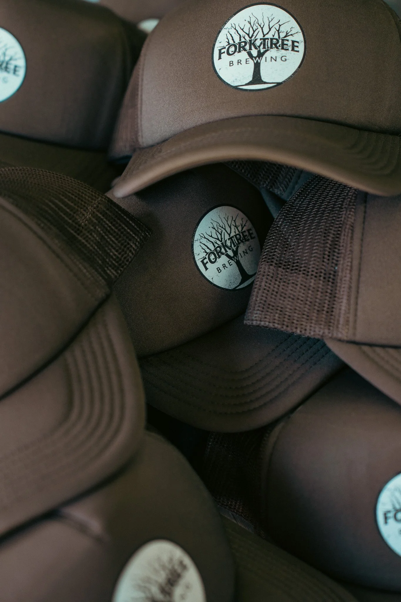 Stacked brown baseball caps with round logos of Fork Tree Brewing featuring a silhouette of a leafless tree.