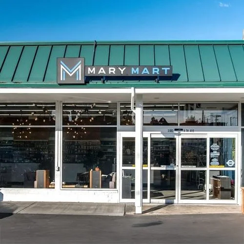 Exterior view of Mary Mart store with large glass windows, green metal roof, and signage.