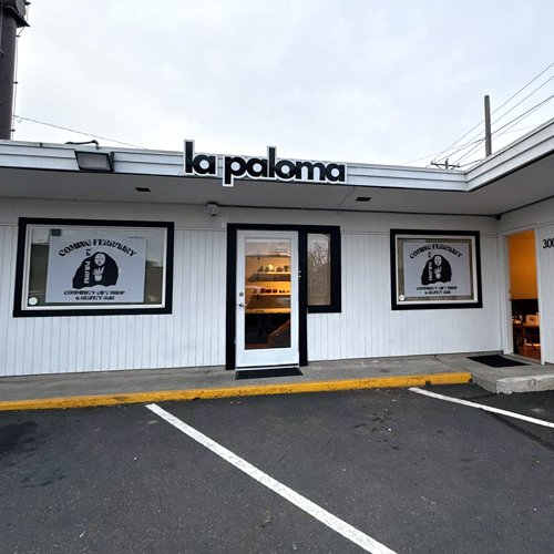 Front of a building with a sign that says 'la paloma' and windows displaying logos for 'Conway/Fayetteville Chamber of Commerce'.