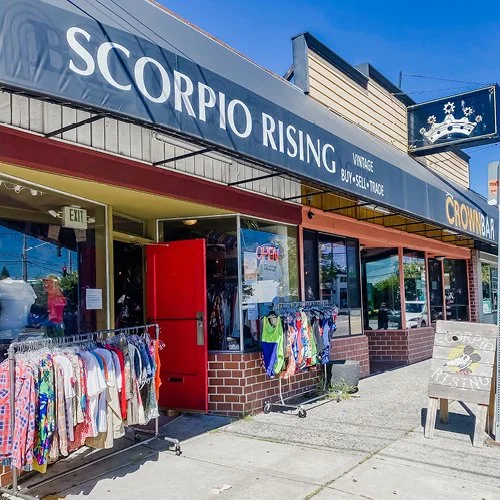 Storefront of Scorpio Rising vintage clothing and buy-sell-trade shop with clothing racks outside and a blue sign with the store name.