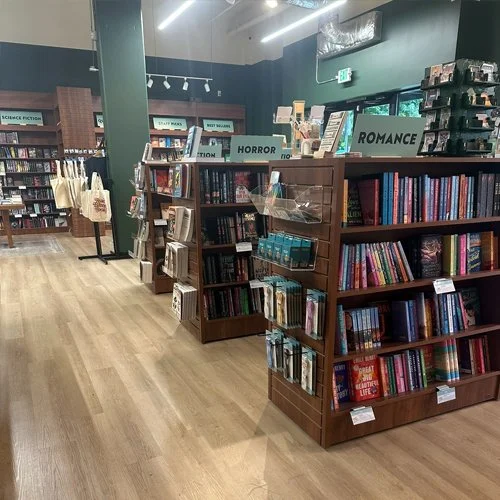 Bookshelves in a bookstore organized by genres labeled Horror, Romance, and Science Fiction, with books and display items.