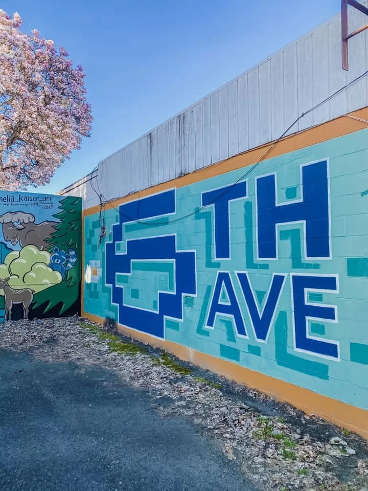 Colorful mural on a wall with the words "Tech Cave" in stylized lettering, next to a tree with pink blossoms and a farm scene with a sheep, a donkey, and a fox.