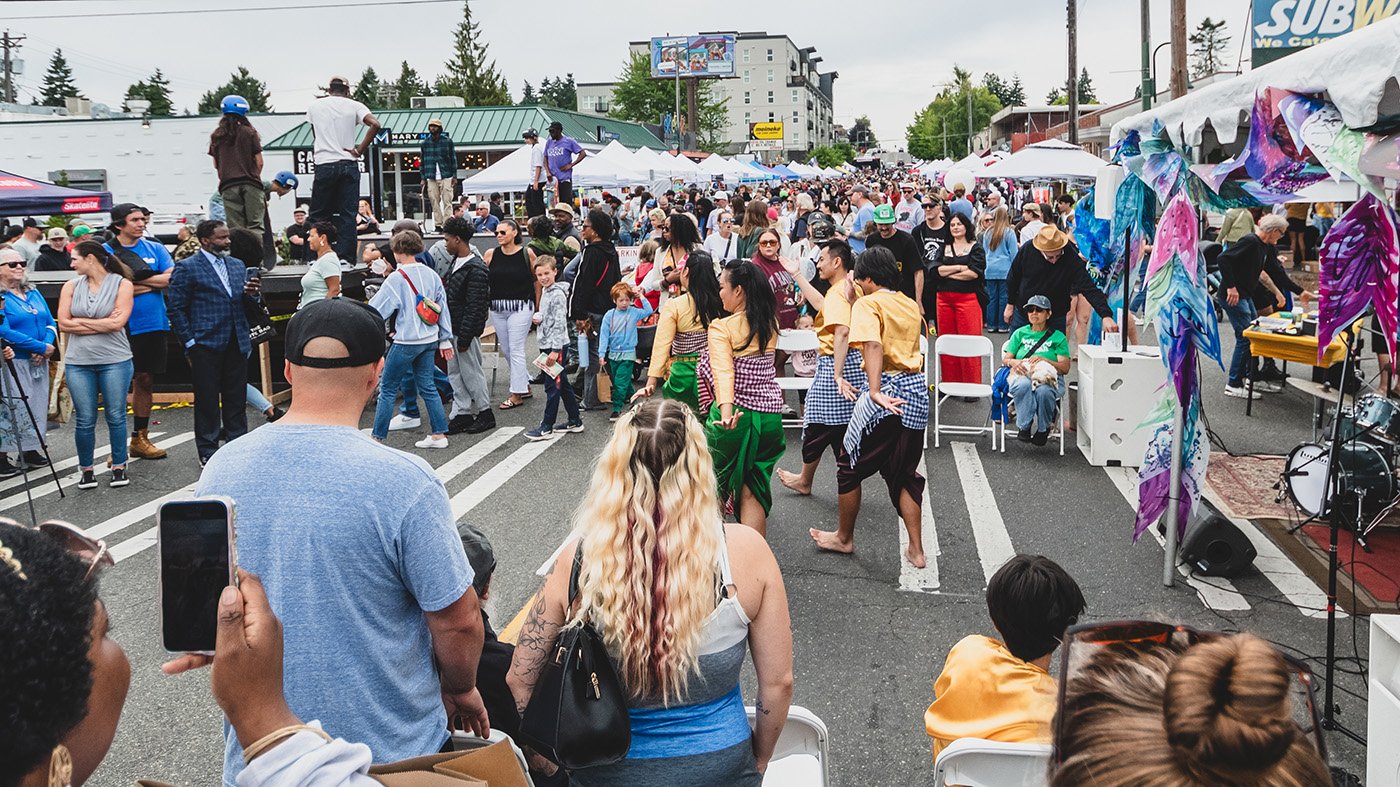 Crowd of people attending an outdoor street festival with vendors and performances.