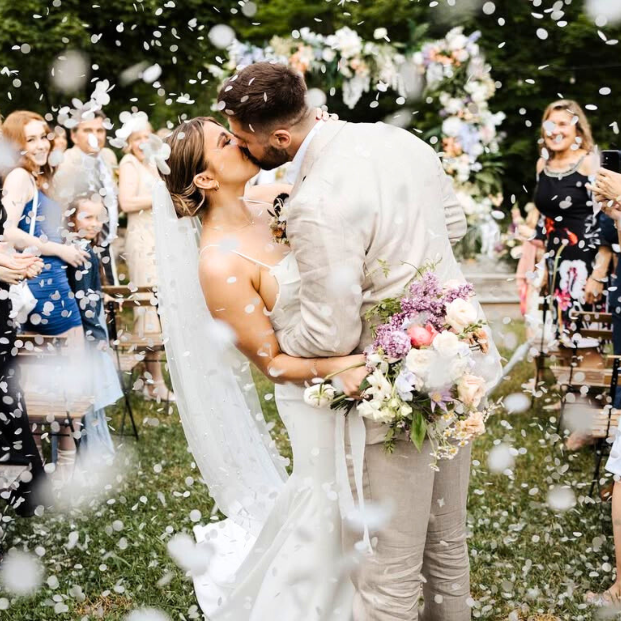 Bride and groom kissing beneath falling white rice paper confetti..png