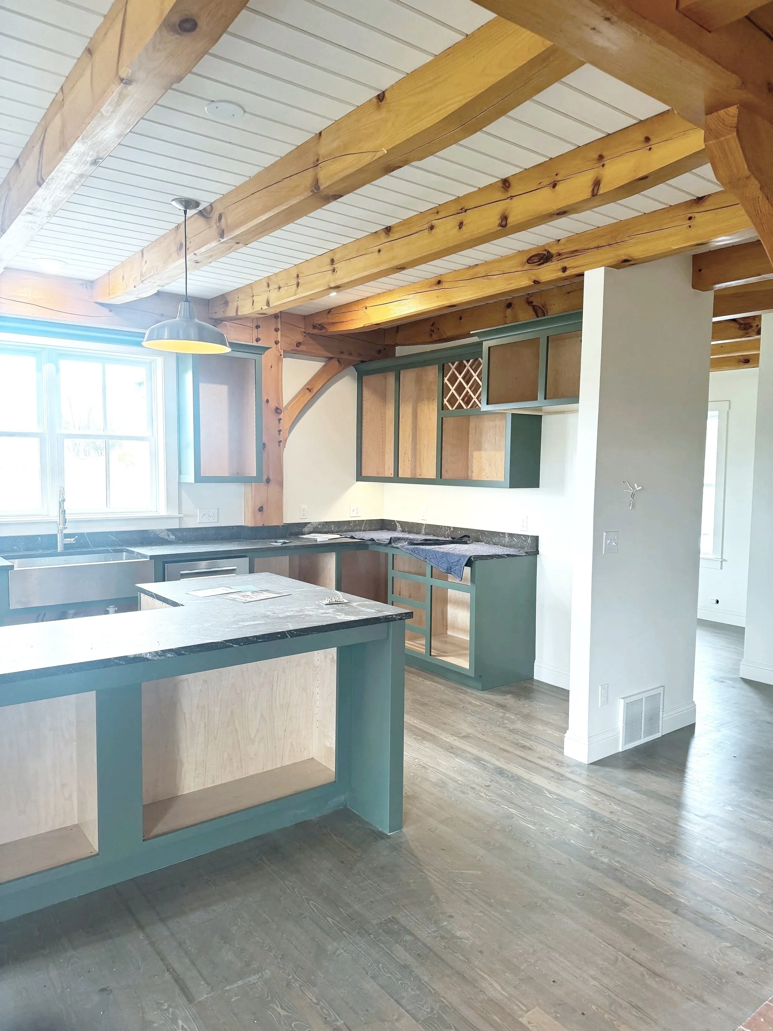 Kitchen full view — painted-in-place custom cabinets, refinished walls, and restored T&G ceiling with exposed beams to tie the entire space together.