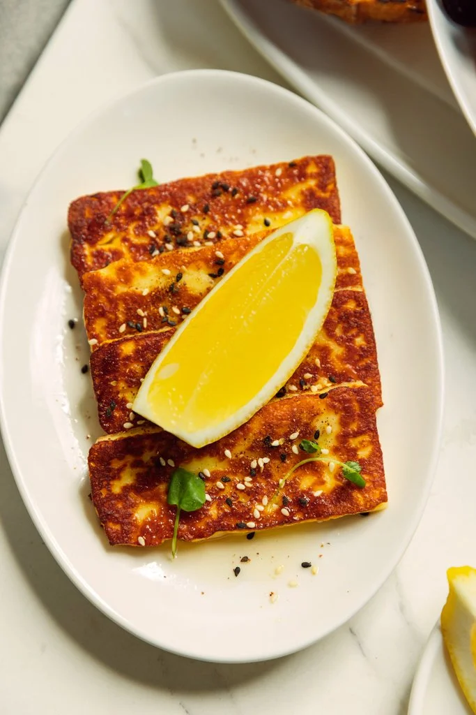 Close-up of Grilled Byron Bay Haloumi with honey, za’atar & lemon on a white oval plate.