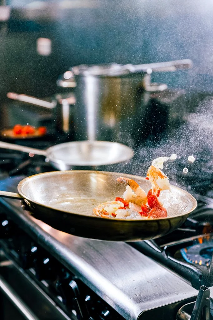 Cooking Sizzling Mooloolaba Prawns with garlic, herbs, chilli, white wine in a stainless steel skillet on a stove.