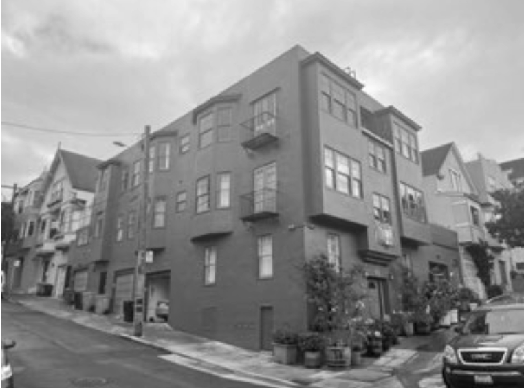 A black and white photo of a corner residential building with multiple windows, small balconies, and potted plants outside.
