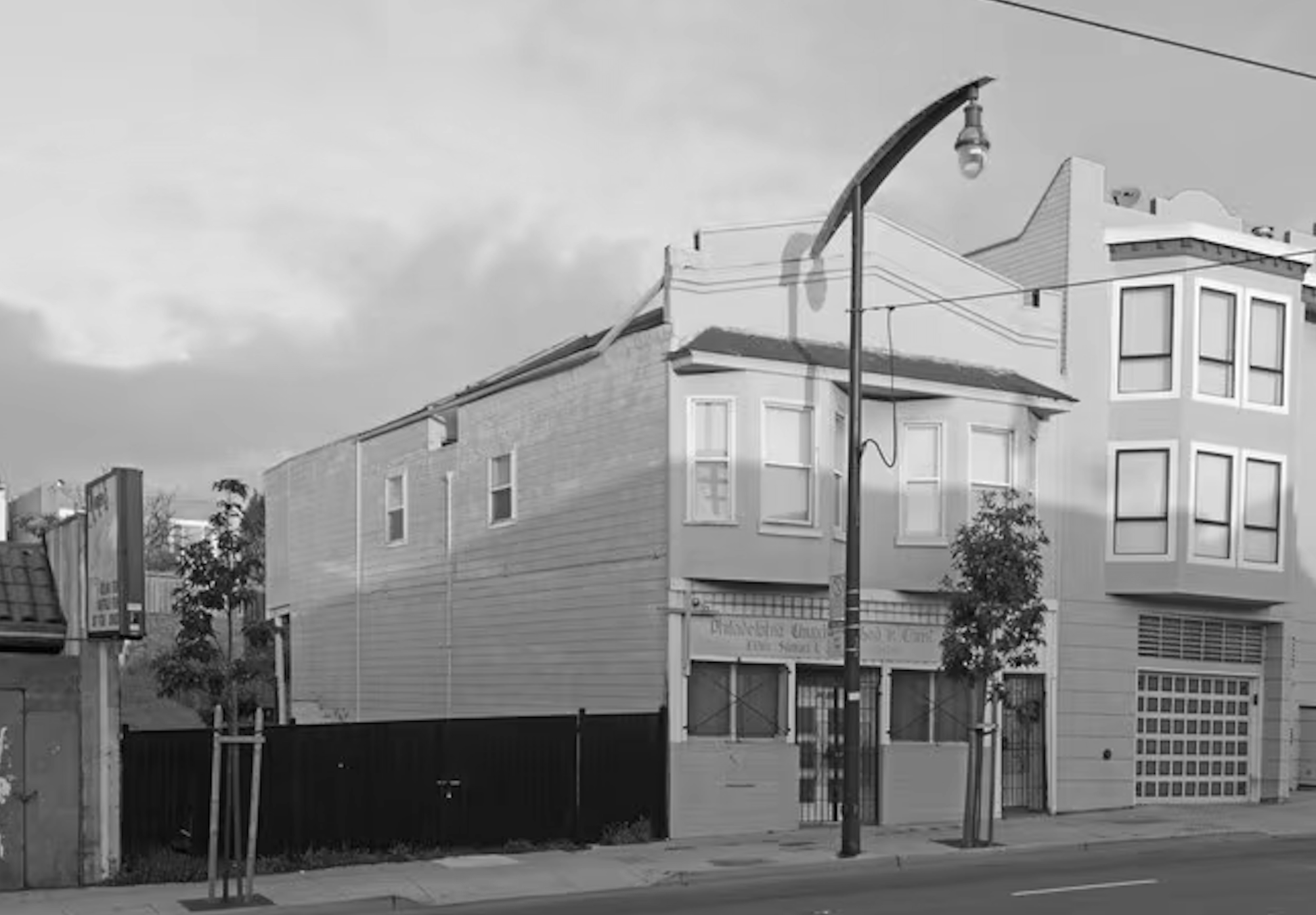 Black and white photo of city street corner with buildings, streetlight, and power lines.