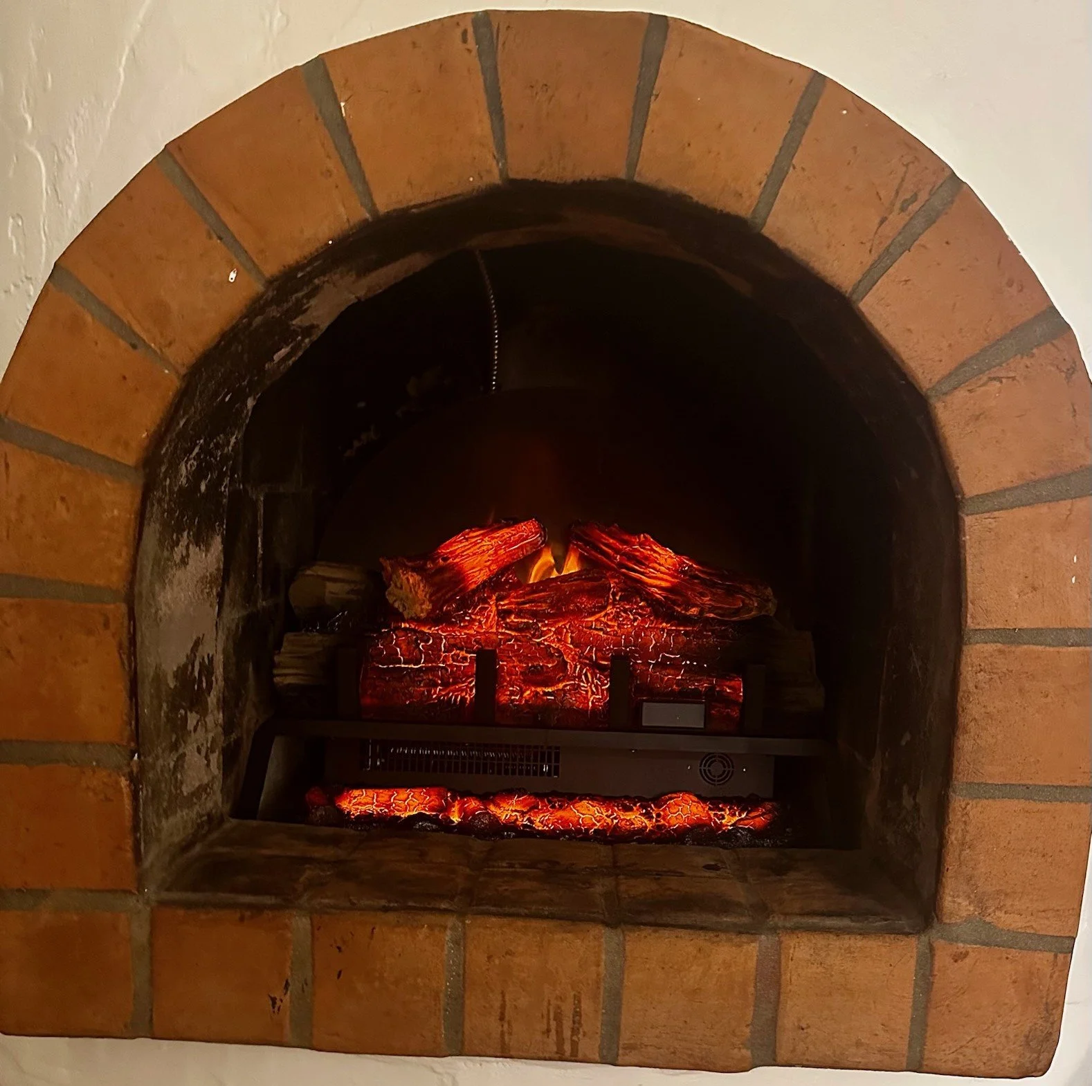 Inside a brick fireplace with glowing red and orange artificial logs and embers.
